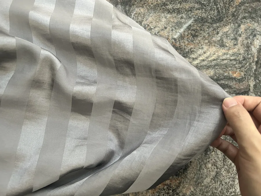 Grey satin fabric with striped sheen held by hand